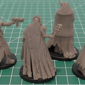 Op de afbeelding: Vier ongeverfde lichtbruine hars miniatuurfiguurtjes op ronde zwarte voetjes. De figuren dragen mantels met capuchon en gewaden, waarbij er &eacute;&eacute;n een pistool vasthoudt, &eacute;&eacute;n een knots met stekels en een andere een lang geweer. Gedetailleerde stoftexturen.