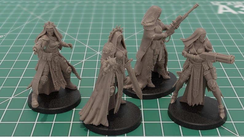 Op de afbeelding: Vier ongeverfde lichtbruine hars miniatuurfiguren op ronde zwarte voetstukken. Elk figuur stelt een krijger voor in een mantel met capuchon en harnas, met diverse wapens waaronder een geweer, een zwaard en een zwaar vuurwapen in actie.