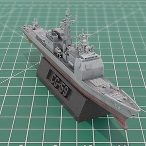 Può includere: Modello dettagliato di una nave da guerra grigia, montato su una base nera. Il modello presenta dettagli intricati, tra cui radar e armi. La base mostra il testo "CG-59". Lo scafo della nave è dipinto in tonalità di grigio e rosso.