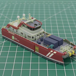 May include: A detailed model of a red and white offshore supply vessel. The model features a detailed deck with containers, cranes, and a bridge. The vessel has the word "Energizer" printed on the side. The model is set on a green grid surface.
