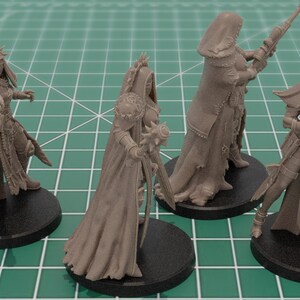 Op de afbeelding: Vier ongeverfde lichtbruine hars miniatuurfiguren op ronde zwarte voetstukken. Elk figuur toont een personage in tactische uitrusting en capuchonmantels, met verschillende wapens zoals een geweer, een strijdhamer en een jachtgeweer.