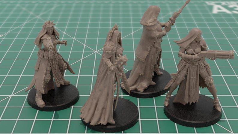 Op de afbeelding: Vier ongeverfde lichtbruine hars miniatuurfiguren op ronde zwarte voetstukken. Elk figuur toont een personage in tactische uitrusting en capuchonmantels, met verschillende wapens zoals een geweer, een strijdhamer en een jachtgeweer.