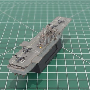 May include: A detailed model of a gray aircraft carrier with several small aircraft on the deck. The model is mounted on a black base and sits on a green grid surface. The number 6 is visible on the deck.