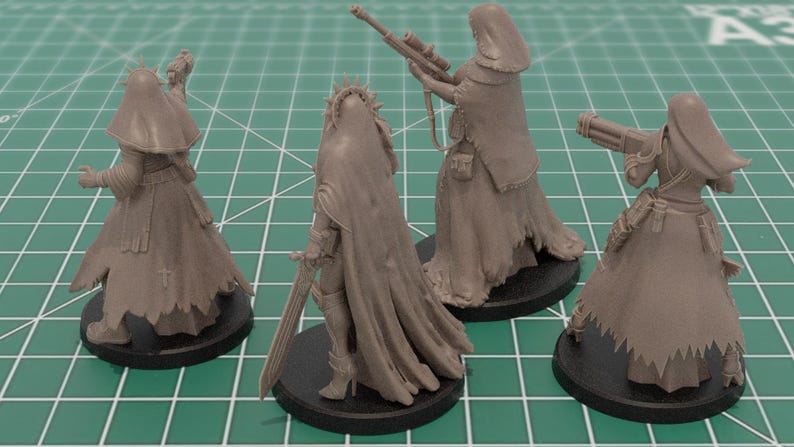 Op de afbeelding: Vier ongeverfde grijze hars miniatuurfiguren op ronde zwarte voetstukken. Elk figuur draagt een mantel met capuchon en een lange rok. De figuren zijn uitgerust met diverse wapens, waaronder een zwaard, een geweer en een zwaar kanon.