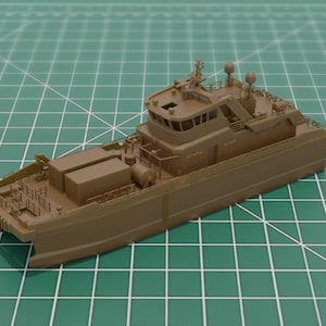 May include: A brown model ship with detailed features, including a bridge, cargo containers, and antennas. The ship is set against a green grid background, suggesting a scale model or a design prototype.