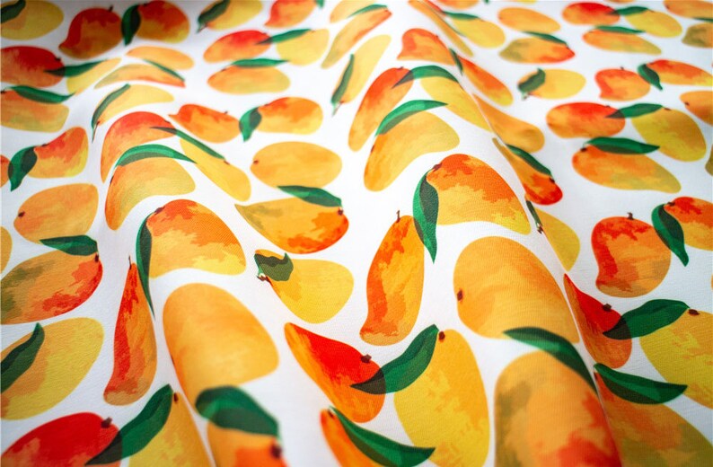 May include: A white fabric with a repeating pattern of yellow and orange mangoes with green leaves.