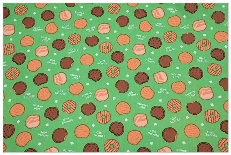 Może przedstawiać: Zielone tło z powtarzającym się wzorem r&oacute;żnych ciasteczek Girl Scout. Ciasteczka obejmują Thin Mints, Samoas i Tagalongs. Tekst "Girl Scouts" i "S'mores" powtarza się w całym wzorze.