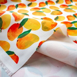 May include: White fabric with a repeating pattern of yellow and orange mangoes with green leaves. The fabric is folded over, showing the white underside.