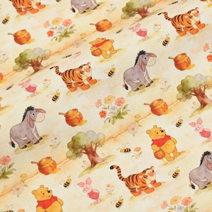 May include: A light yellow fabric featuring a repeating pattern of Winnie the Pooh characters including Tigger, Eeyore, Piglet, and Pooh Bear. The design includes illustrations of honey pots, small bees, green trees, and colourful flowers.