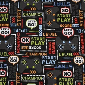 May include: Black fabric with a repeating pattern of video game controllers, speech bubbles with "LET'S GO!", and text like "START PLAY", "LEVEL", and "CHAMPION". The design includes red, green, and yellow accents.