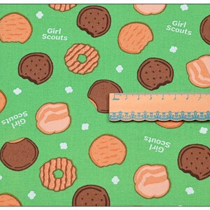 Może przedstawiać: Zielony materiał z powtarzającym się wzorem ciasteczek Girl Scout. Ciasteczka są w r&oacute;żnych kształtach i kolorach, w tym czekoladowe, maślane i z masłem orzechowym.