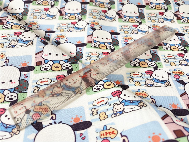 May include: White fabric with a repeating pattern of a cartoon dog wearing a blue shirt and holding a yellow chick. The dog is surrounded by a blue and white border with the words "Chubby" and "Hi-m" in a speech bubble. The fabric is measured with a ruler in inches.