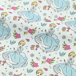 May include: Pale blue fabric with a repeating pattern of Cinderella in her ball gown, mice, birds, flowers, and stars. The illustrations are in a cartoon style, with a soft colour palette of blue, pink, and yellow on a white background.