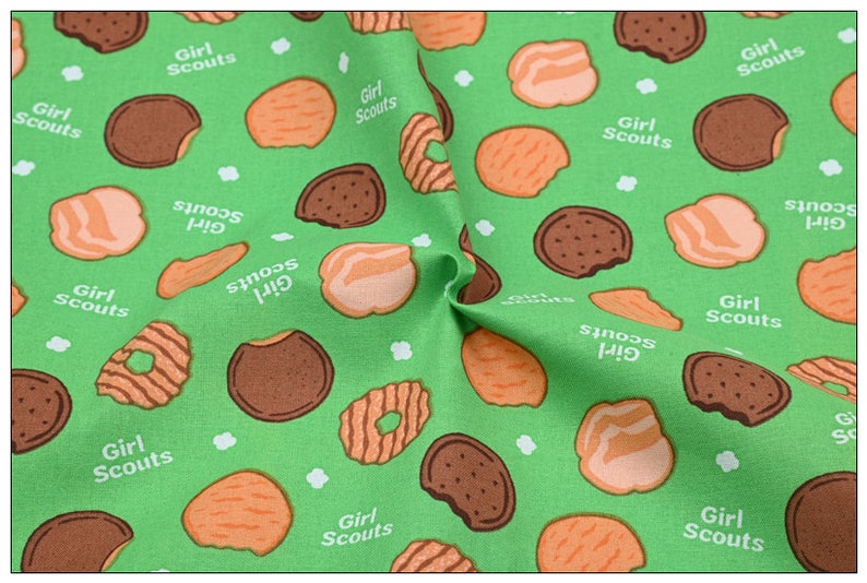 Może przedstawiać: Zielony materiał z powtarzającym się wzorem ciasteczek Girl Scout. Ciasteczka są w r&oacute;żnych kształtach i kolorach, w tym czekoladowe, maślane i z masłem orzechowym.