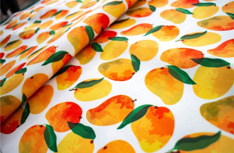 May include: White fabric with a repeating pattern of yellow and orange mangoes with green leaves.