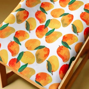 Może przedstawiać: Biała tkanina z powtarzającym się wzorem żółtych i pomarańczowych mango. Tkanina jest drapowana na drewnianym krześle.
