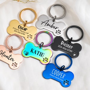 May include: Five different dog bone-shaped pet ID tags with engraved names and phone numbers. The tags are in various colors, including gold, silver, black, blue, and rainbow.