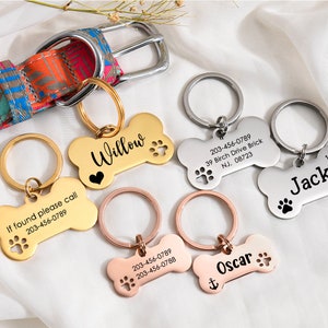 May include: Four personalized dog bone-shaped tags with engraved names and phone numbers. The tags are gold, silver, and rose gold. The tags are attached to key rings.