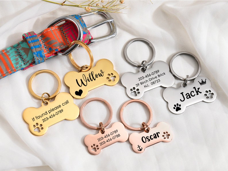May include: Four personalized dog bone-shaped tags with engraved names and phone numbers. The tags are gold, silver, and rose gold. The tags are attached to key rings.
