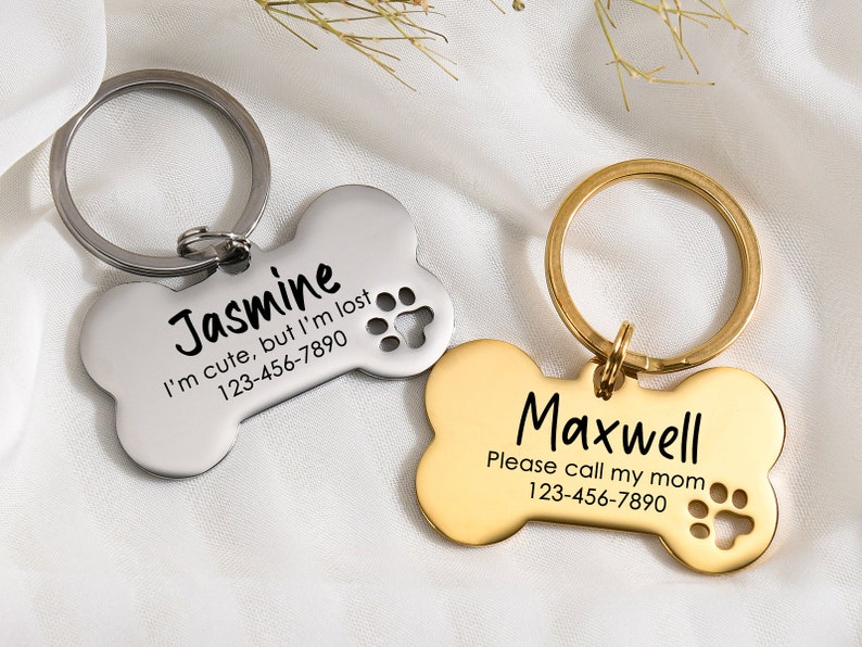 May include: Two bone-shaped dog tags with engraved text and paw prints. The silver tag reads "Jasmine I'm cute, but I'm lost 123-456-7890". The gold tag reads "Maxwell Please call my mom 123-456-7890".