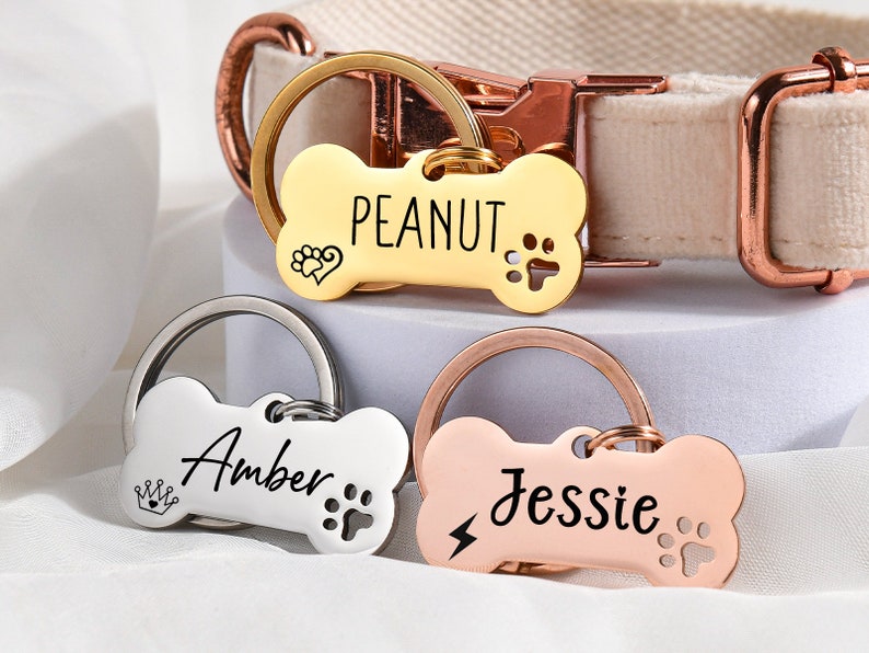 May include: Three dog bone-shaped name tags with different names engraved on them. The tags are attached to key rings. The names on the tags are "Peanut", "Amber", and "Jessie".