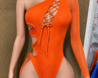 May include: A bright orange one-piece bodysuit featuring an asymmetrical one-shoulder design, a long sheer sleeve on the left side, and a lace-up cutout detail on the chest and right side with matching orange ties and a high-cut leg opening.
