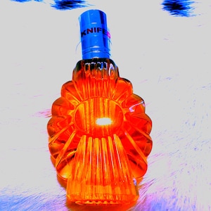 May include: An orange-colored, decorative glass bottle with a blue cap. The word "KNIFE" is printed on the cap. The bottle has a unique, flower-like design with vertical ridges. The bottle is likely used for decorative purposes.