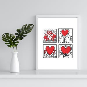 May include: A framed art print featuring four square panels with Keith Haring-style illustrations. Each panel has black outlines and red figures, including hearts and dancing figures. The print is displayed on a white shelf.