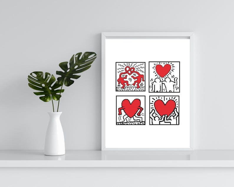 May include: A framed art print featuring four square panels with Keith Haring-style illustrations. Each panel has black outlines and red figures, including hearts and dancing figures. The print is displayed on a white shelf.
