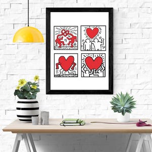 May include: A framed art print featuring four panels with Keith Haring-style illustrations. The artwork includes red figures and hearts on a white background, framed in black. The print is displayed on a light wood table with decorative items.