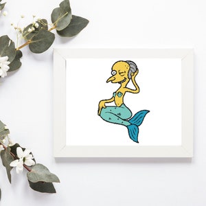 May include: A framed print featuring a cartoon character as a mermaid. The character has yellow skin, a blue tail, and is wearing a seashell bra. The print is in a white frame, and the background is white. Decorative flowers and greenery surround the frame.