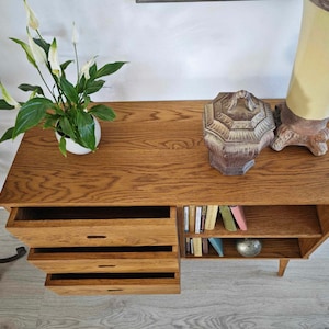 May include: A wooden cabinet with four drawers and a shelf. The cabinet has a light brown finish and is decorated with a small, decorative pot and a ceramic box.