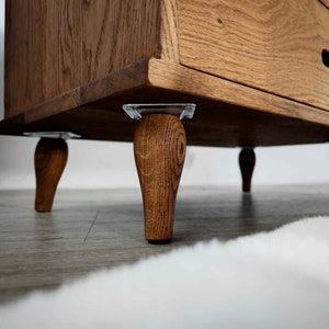 May include: A wooden dresser with four turned legs and a single drawer. The dresser is made of a light brown wood with a natural finish.