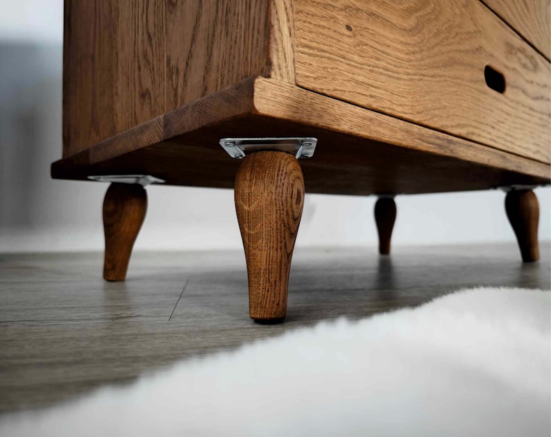 May include: A wooden dresser with four turned legs and a single drawer. The dresser is made of a light brown wood with a natural finish.