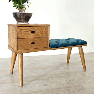 Op de afbeelding: Een houten bank met een teal gecapitonneerde zitting en twee laden. De bank heeft een mid-century modern stijl.