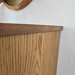 May include: Close-up of the top edge of a wooden cabinet with a light brown stain. The wood grain is visible and the cabinet has a slightly rounded edge.