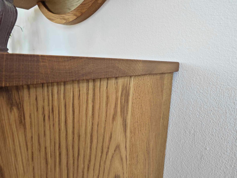 May include: Close-up of the top edge of a wooden cabinet with a light brown stain. The wood grain is visible and the cabinet has a slightly rounded edge.