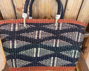 Könnte beinhalten: Gewebte Tragetasche mit geometrischem Muster in Schwarz, Orange und Creme. Die Tasche hat schwarze Ledergriffe und steht auf einem Holzstuhl. Die Tasche ist rechteckig und scheint handgefertigt zu sein.