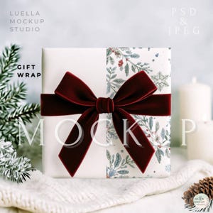 以下が含まれることがあります： バーガンディ色のベルベットのリボンが付いた、包装されたギフト。 ギフト包装は白で、片側に花柄があります。 画像には「GIFT WRAP」と「MOCKUP」というテキストが含まれています。