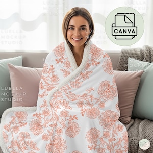 May include: A white blanket with an orange floral pattern, wrapped around a person. The blanket has a soft, sherpa-like trim. The image also includes pillows in shades of pink and blue.