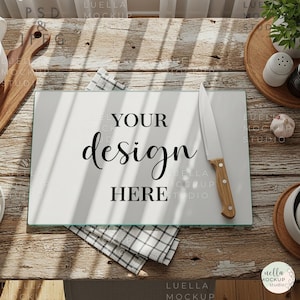 May include: A rectangular glass cutting board with the text "YOUR design HERE" is displayed on a rustic wooden table. A knife with a wooden handle rests on the board, alongside a checkered cloth.