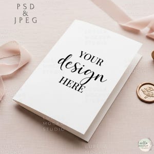 May include: A white card with the text "YOUR design HERE" in black script. The card is slightly angled, with a soft pink ribbon and a gold wax seal in the background. The image is a mockup.