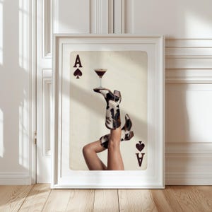 Pode incluir: Impress&atilde;o art&iacute;stica emoldurada com um design de carta de jogar &Aacute;s de Espadas. A imagem mostra um par de botas de cowgirl com um padr&atilde;o preto e branco, segurando um copo de cocktail. A obra de arte &eacute; definida contra um fundo neutro.