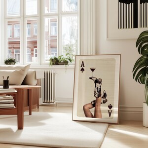 Pode incluir: Uma impress&atilde;o de arte emoldurada com um copo de cocktail equilibrado em pernas com botas estampadas em preto e branco. A obra de arte &eacute; exibida numa sala de estar com um sof&aacute;, uma mesa de centro e uma grande planta em vaso.