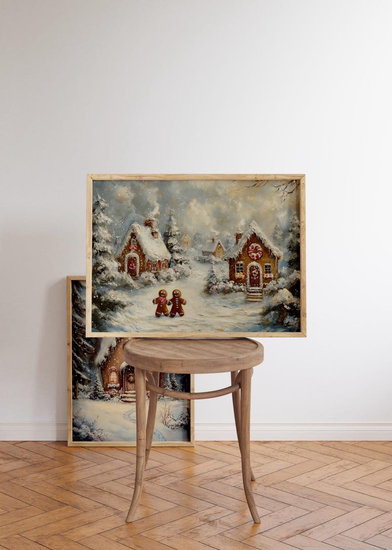 May include: A framed winter landscape painting featuring snow-covered gingerbread houses and two gingerbread people. The artwork has a warm, inviting color palette with a wooden frame, evoking a cozy holiday theme. The painting is displayed on a wooden stool.