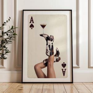 Pode incluir: Impress&atilde;o art&iacute;stica emoldurada com um design de &Aacute;s de Espadas. A imagem mostra botas de cowgirl com um padr&atilde;o preto e branco segurando um copo de coquetel. As botas est&atilde;o de cabe&ccedil;a para baixo, com as pernas estendidas para cima. Moldura preta.