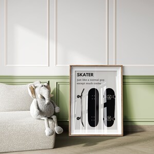 May include: A framed print featuring the word "SKATER" above the phrase "just like a normal guy, except much cooler." The print displays two black skateboards. A stuffed elephant toy sits on a white textured couch.