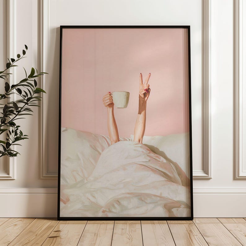 May include: Framed art print featuring a person's arms reaching up from under a white blanket. One hand holds a white mug, the other makes a peace sign. The background is a solid pink color.