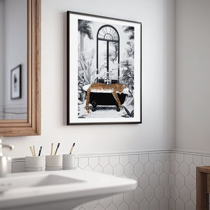 May include: A framed wall art print featuring a black and white illustration of a leopard resting in a clawfoot bathtub. The scene includes tropical plants and an arched window in the background. The leopard has a spotted orange and black coat.