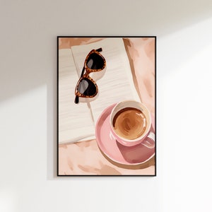 K&ouml;nnte beinhalten: Eine rosa Kaffeetasse mit braunem Kaffee darin, eine braune Sonnenbrille und ein wei&szlig;es Buch auf einer rosa und braunen Oberfl&auml;che.
